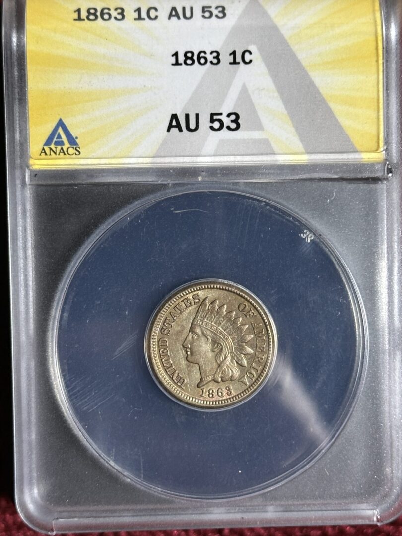 An 1863 Indian Head Cent ANACS AU53, displayed in a protective case against a yellow and blue background.